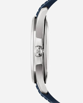 Side view of the Patek Philippe Nautilus in silver with a blue strap, highlighting the watch’s thickness and a crown engraved with an emblem against a plain, light-colored background.