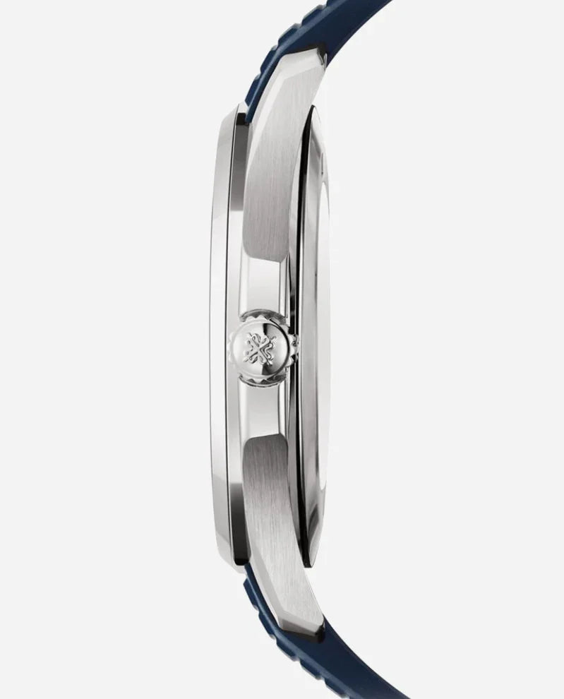 Side view of the Patek Philippe Nautilus in silver with a blue strap, highlighting the watch’s thickness and a crown engraved with an emblem against a plain, light-colored background.